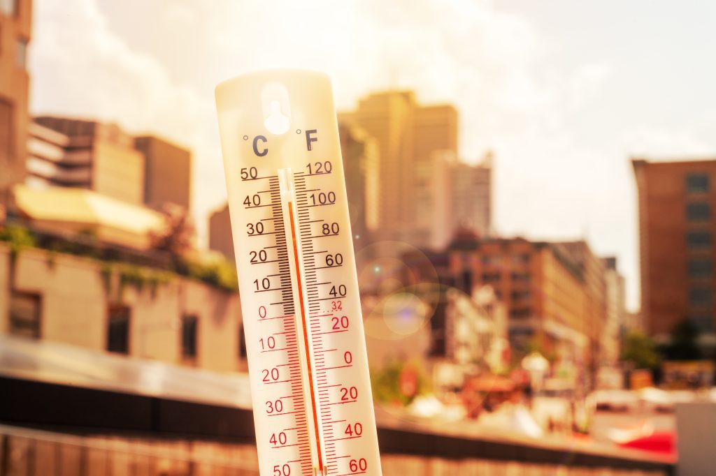 Photo of a thermometer with mercury rising past 100 degrees Fahrenheit in front of a city street backdrop