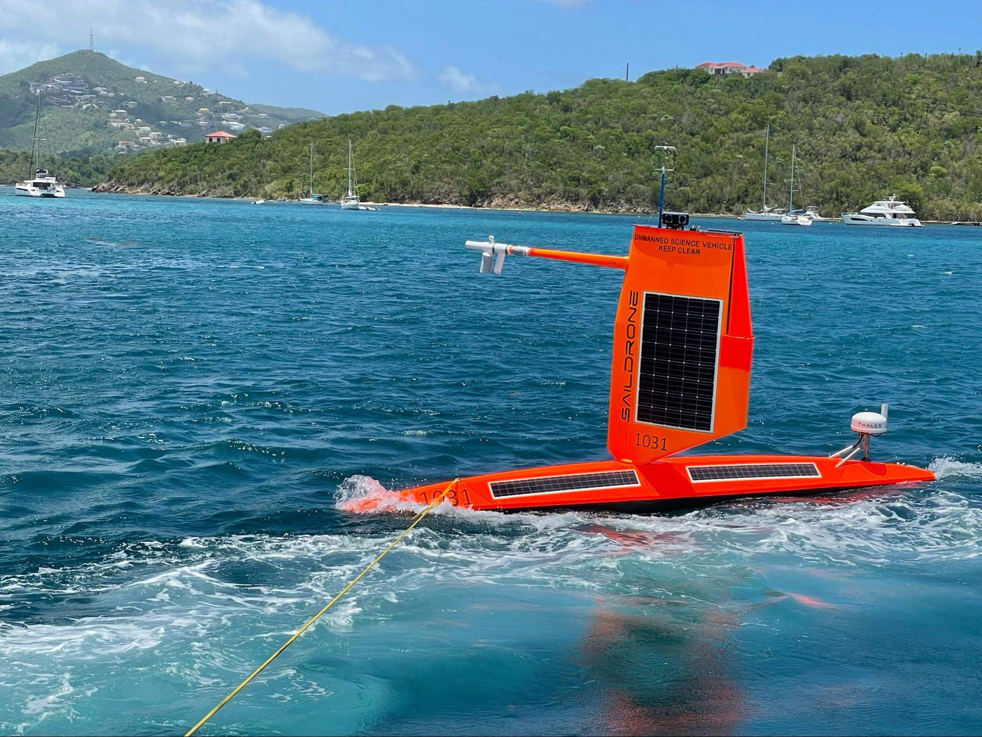Red autonomous glider in the shape of a surfboard with a sail is connected to a towline for deployment