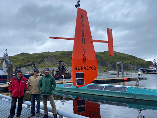 Image of three men in front of the Saildrone Surveyor before it was deployed to collect data at sea. 