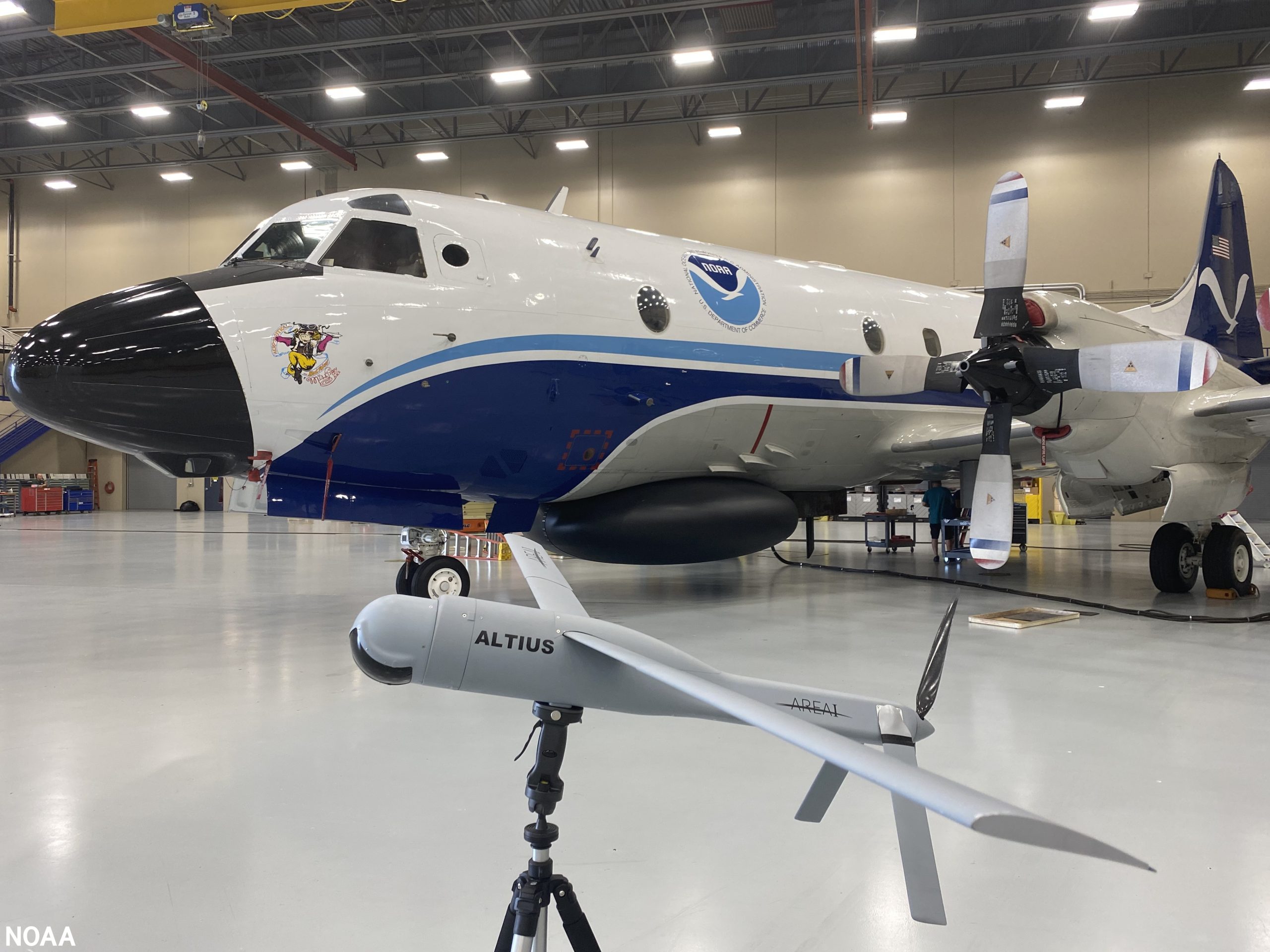 An Altius-600 uncrewed aircraft system demonstration model appears in front of an Hurricane Hunter NOAA WP-3D Orion at NOAA's Aircraft Operations Center in Lakeland, Florida.