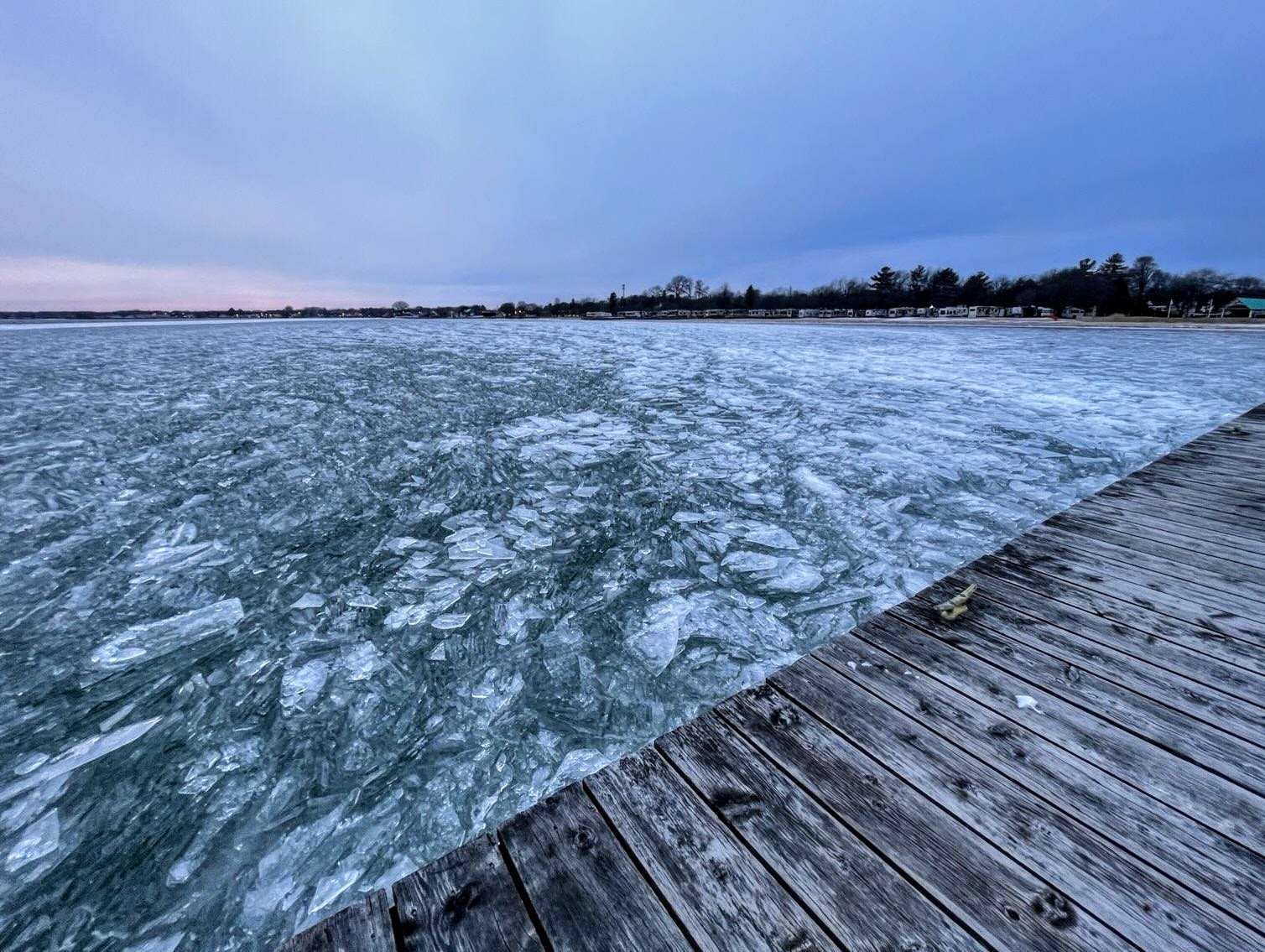 A wooden dock is surrounded by sharp shards of ice on a lake