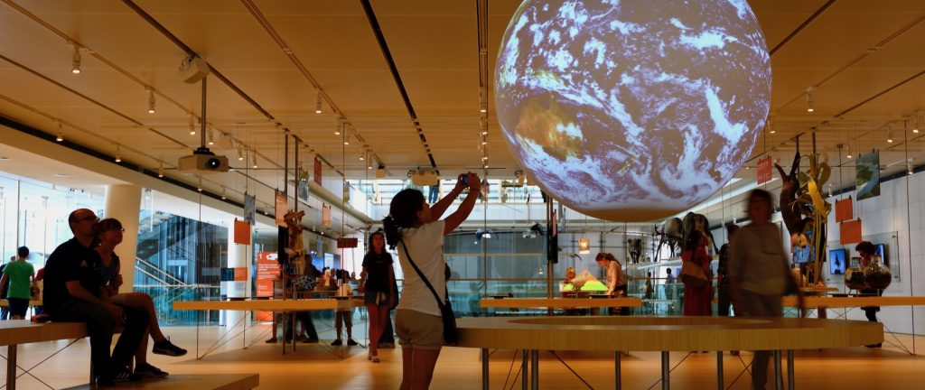 A girl takes a photo of the Science on a Sphere globe displayed in a museum exhibit.