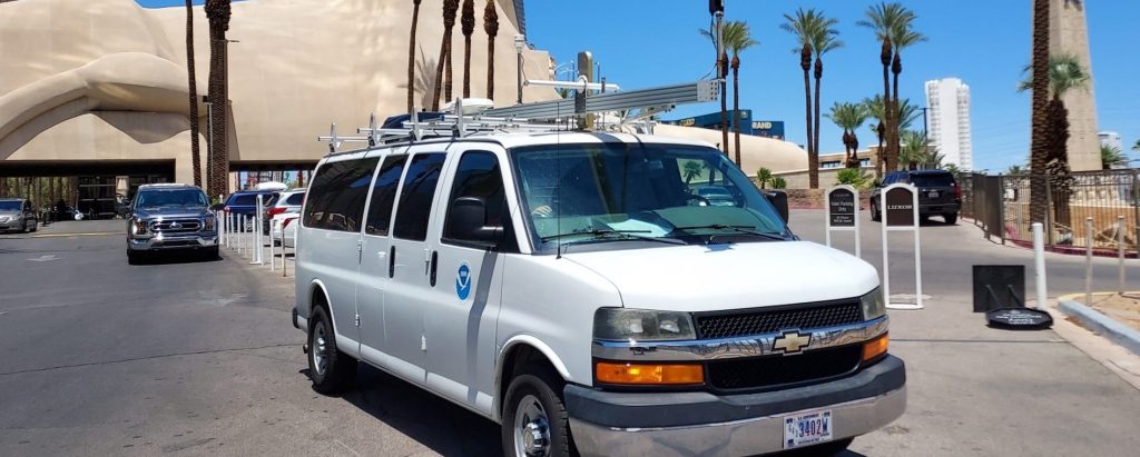 A photo of a white Chevrolet van equipped with air quality instruments parked in front of the Luxor Casino and Hotel in Las Vegas, Nevada.