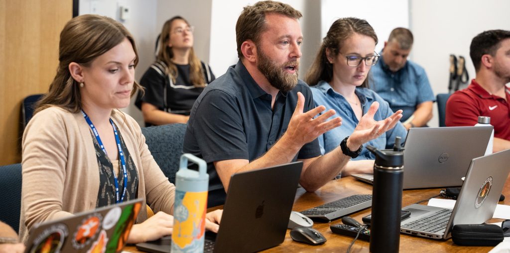 A scientists flanked by two female colleagues gestures with his hands as he makes a point during a review of a technical evaluation of two experimental fire weather tools.